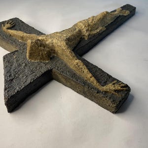 May include: A dark gray ceramic cross with a raised, light brown figure of a person on it.
