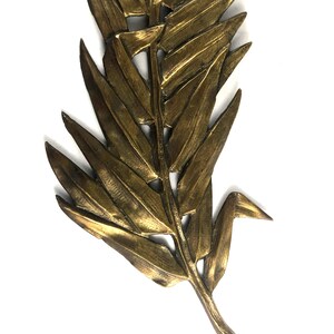 May include: A gold-colored metal leaf wall decor with a detailed design. The leaf is made of a single piece of metal and has a realistic appearance.