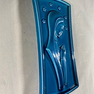 May include: A blue ceramic wall plaque with a raised image of a woman in prayer. The plaque is decorated with white stars.