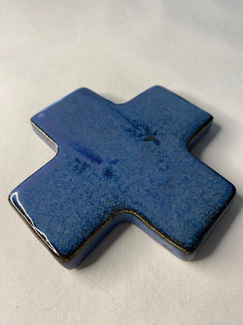 K&ouml;nnte beinhalten: Ein blaues Keramikkreuz mit leicht strukturierter Oberfl&auml;che. Das Kreuz hat eine dunkelblaue Glasur mit einem leichten Metallic-Glanz.