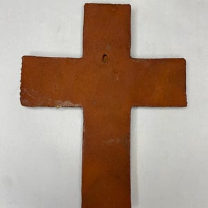 May include: A terracotta cross with a hole in the center for hanging. The cross is a rustic brown color and has a slightly uneven surface.