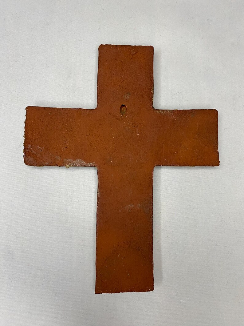 May include: A terracotta cross with a hole in the center for hanging. The cross is a rustic brown color and has a slightly uneven surface.