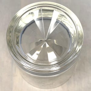 Puede incluir: Vaso de vidrio transparente con base facetada. La parte inferior del vaso presenta un dise&ntilde;o de estrella, con l&iacute;neas que irradian desde el centro. El vaso es cil&iacute;ndrico con un borde ligeramente ensanchado.