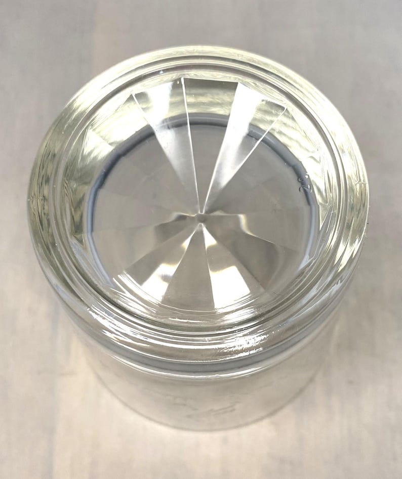 Puede incluir: Vaso de vidrio transparente con base facetada. La parte inferior del vaso presenta un dise&ntilde;o de estrella, con l&iacute;neas que irradian desde el centro. El vaso es cil&iacute;ndrico con un borde ligeramente ensanchado.