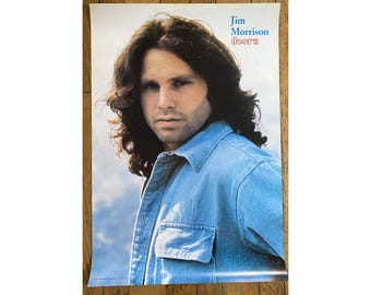 May include: A vintage poster featuring a close-up portrait of Jim Morrison, the lead singer of The Doors. He is wearing a blue denim shirt and has long, dark hair. The poster has the text "Jim Morrison Doors" at the top.