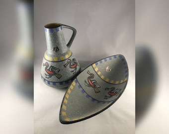 May include: A set of two ceramic serving pieces with a blue and yellow geometric pattern and stylized bird illustrations. The pieces are a pitcher and a shallow oval dish.