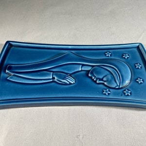 May include: A blue ceramic wall plaque with a raised image of a woman in a blue robe with stars around her head.