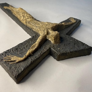 May include: A ceramic wall sculpture of a crucifix with a textured black background and a light brown figure of Jesus Christ.