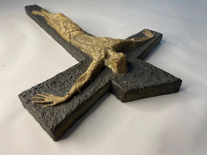 May include: A ceramic wall sculpture of a crucifix with a textured black background and a light brown figure of Jesus Christ.