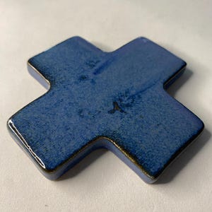 K&ouml;nnte beinhalten: Ein blaues Keramikkreuz mit leicht strukturierter Oberfl&auml;che. Das Kreuz ist ein schlichtes Design mit leicht abgerundeten Kanten.