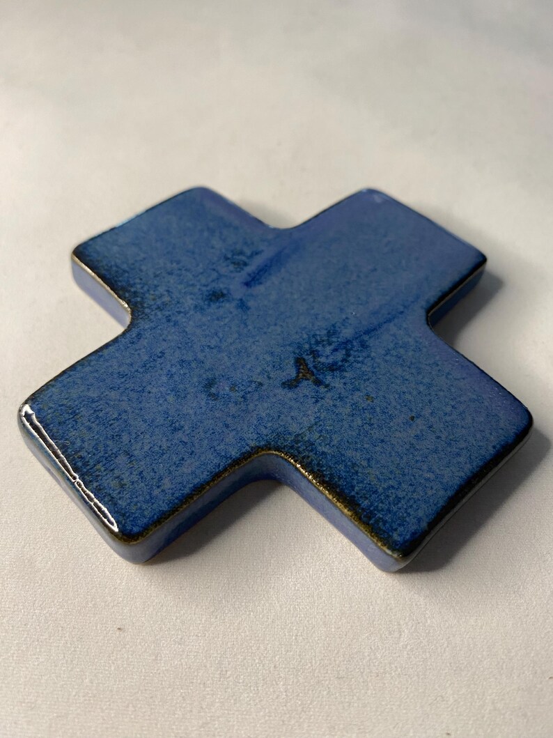 K&ouml;nnte beinhalten: Ein blaues Keramikkreuz mit leicht strukturierter Oberfl&auml;che. Das Kreuz ist ein schlichtes Design mit leicht abgerundeten Kanten.