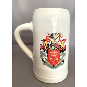 May include: White ceramic beer stein with a red, green and gold crest featuring a bird and the text "DOCTRINA PROMOVERE NATURAM".