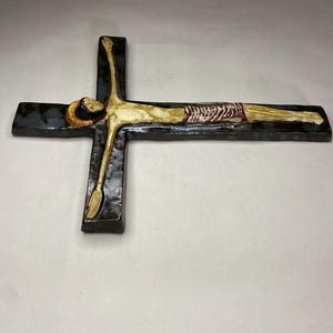 Może przedstawiać: Ceramiczny krucyfiks ścienny z niebieską i czarną glazurą. Postać Jezusa jest pomalowana na biało i ż&oacute;łto z czerwono-białym prześcieradłem.
