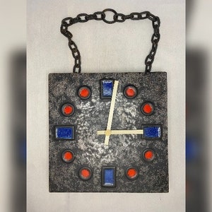 May include: A black ceramic clock with a silver face and red and blue accents. The clock has a chain hanging from the top.