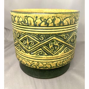 May include: A decorative ceramic planter in yellow and green. The planter has detailed geometric and floral patterns in dark green on a yellow surface. The base is a solid dark green colour. The planter is suitable for indoor plants.