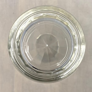 Puede incluir: Un vaso transparente, visto desde abajo, con un exterior texturizado y estriado y un interior geom&eacute;trico y facetado. El vaso est&aacute; dise&ntilde;ado para beber, con una apariencia transparente. El vaso tiene forma circular.