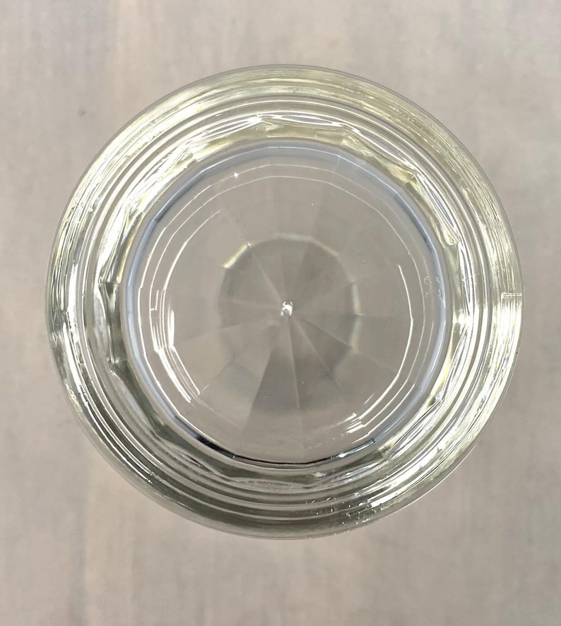 Puede incluir: Un vaso transparente, visto desde abajo, con un exterior texturizado y estriado y un interior geom&eacute;trico y facetado. El vaso est&aacute; dise&ntilde;ado para beber, con una apariencia transparente. El vaso tiene forma circular.