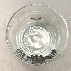 May include: Clear, round whiskey glass with a thick base. The glass has the words "Tennessee Whiskey" printed in black, and a black graphic design at the bottom. The glass is empty.