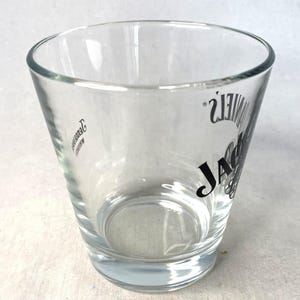May include: A clear shot glass with a tapered design, featuring the "JACK DANIEL'S" logo in black. The glass has a sturdy base and a slightly flared rim. The logo is printed on the side. Ideal for serving spirits, this glass is a classic.