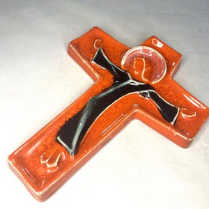 May include: Orange ceramic wall cross with a black and white figure of Jesus Christ in relief.