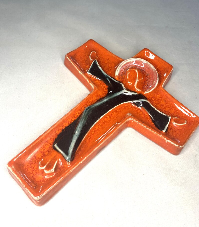 May include: Orange ceramic wall cross with a black and white figure of Jesus Christ in relief.