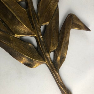 May include: A gold-colored metal leaf sculpture with a detailed design. The leaf has a long stem and is made of thin metal.