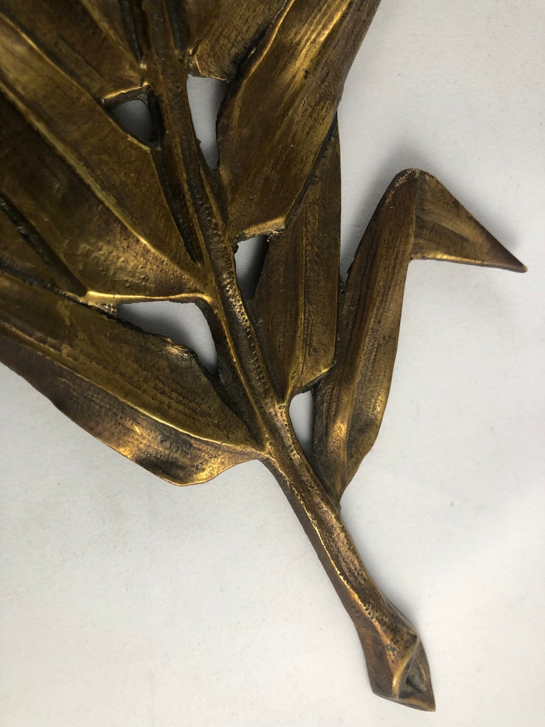 May include: A gold-colored metal leaf sculpture with a detailed design. The leaf has a long stem and is made of thin metal.