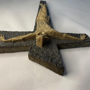 May include: A ceramic wall sculpture of a crucifix with a textured, dark gray cross and a light brown figure of Jesus Christ.