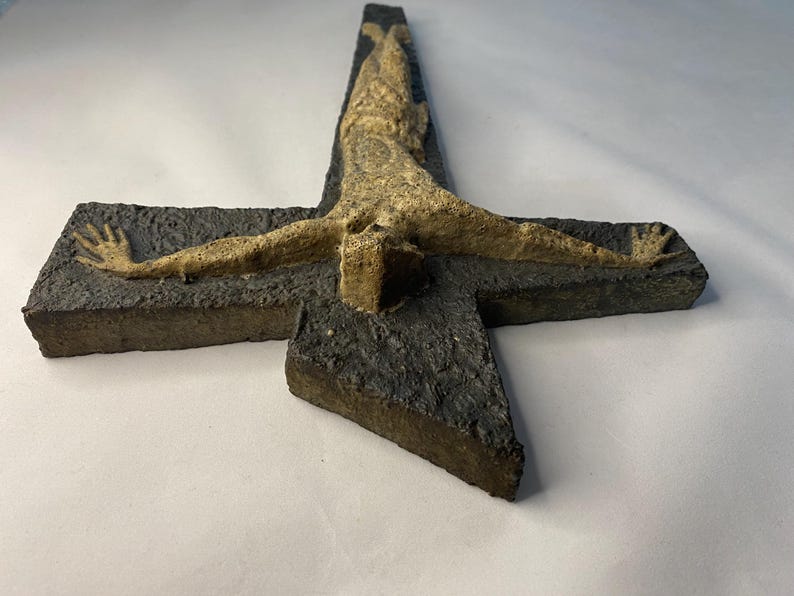 May include: A ceramic wall sculpture of a crucifix with a textured, dark gray cross and a light brown figure of Jesus Christ.