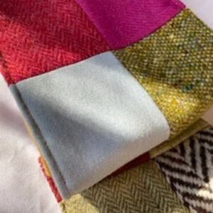 May include: A patchwork scarf made of different colored fabrics, including red, pink, green, and blue. The scarf is made of a soft, textured material.