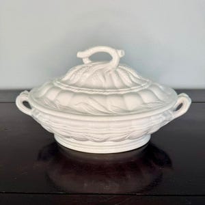 以下が含まれることがあります： 白いセラミック製のサービングディッシュ、蓋付き。 皿には、小麦と葉の精巧なエンボス加工が施されています。 蓋にはループハンドルが付いています。 皿には両側にハンドルが2つ付いています。 全体的な形状は楕円形です。