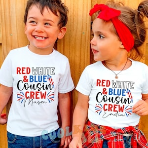 May include: Two children wearing white t-shirts with red, white, and blue text that says "Red White & Blue Cousin Crew" with a firework graphic and their names, Mason and Emilia.