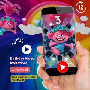 May include: A smartphone screen displaying a birthday video invitation featuring a pink cartoon character with blue eyes and a flower crown. The video is set against a colorful background with a rainbow and clouds. The text on the screen reads "3" and "12 HOURS".