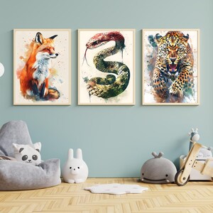 May include: Three framed watercolor animal prints. The prints feature a fox, a snake, and a leopard. The fox is orange and white, the snake is green and red, and the leopard is brown and black. The frames are a light wood color.