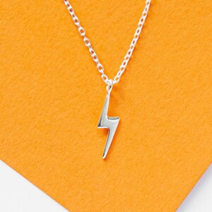 May include: A silver necklace with a lightning bolt pendant against an orange background.