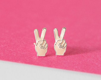 May include: A pair of silver peace sign earrings with a light pink enamel finish.