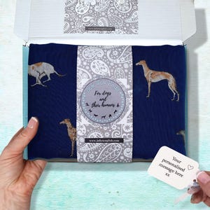 May include: A navy blue fabric featuring greyhound dog illustrations is displayed in an open box. The box interior has a paisley pattern, and a tag reads "Your personalised message here". The text "Bow Wow Haus" is also visible.