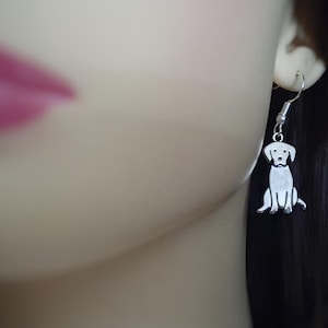 May include: Silver dog-shaped dangle earring. The earring features a detailed outline of a sitting dog with a small loop for the ear wire. The dog's features include a head, body, and legs. The earring is attached to a silver fish hook.