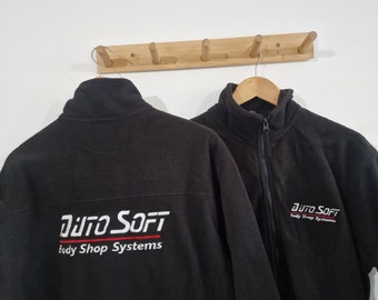 May include: Two black fleece jackets with the logo "AUTO SOFT Body Shop Systems" embroidered on the back. The jackets are hanging on a wooden rack.