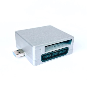 Puede incluir: Un dispositivo electrónico de color plateado con un conector USB y un puerto verde oscuro. El dispositivo tiene una superficie texturizada y el número "1" está impreso en el lateral. Probablemente se utiliza para conectarse a un ordenador.