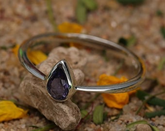 May include: A silver ring with a teardrop-shaped purple gemstone set in the center.