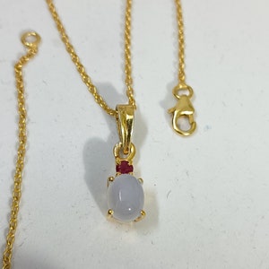 May include: A gold chain necklace with a pendant featuring a white oval gemstone and a small red gemstone accent.