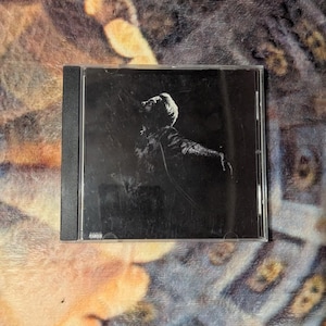 May include: A black and white CD case featuring a silhouette of a person with their arms outstretched. The image has a dark, moody aesthetic. The CD case is in a standard jewel case.