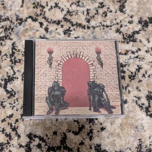 May include: A CD case featuring an illustration of a brick archway with a red door. Two figures in armor are positioned on either side of the archway. Two torches are on the wall. The artwork has a vintage, fantasy theme.