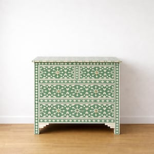 Può includere: Cassettiera a fantasia floreale verde e bianca con quattro cassetti. Il mobile ha una forma rettangolare con un piano piatto ed è realizzato in legno. I cassetti sono decorati con un motivo floreale ripetuto. Il mobile è appoggiato a un muro bianco.