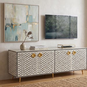 Könnte beinhalten: Ein modernes Wohnzimmer mit einem schwarz-weiß gemusterten Schrank mit goldenen Griffen. Über dem Schrank befindet sich ein gerahmtes abstraktes Gemälde und ein montierter Fernseher. Eine Vase mit einer Pflanze und Bücher stehen auf dem Schrank.