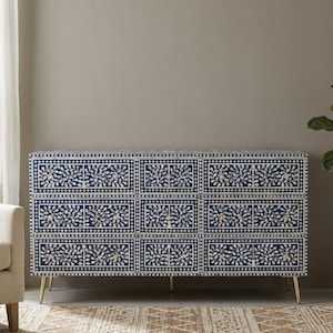 Könnte beinhalten: Eine rechteckige Kommode mit neun Schubladen in Dunkelblau mit kunstvollen weißen Blumen- und Rankenintarsien. Das Möbelstück ist von einem geometrischen Rand umgeben und steht auf vier schlanken, konischen goldfarbenen Metallbeinen.