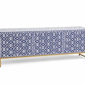 May include: A long, rectangular cabinet with a geometric blue and white pattern. The cabinet has three doors and sits on a gold-colored metal frame. The design is repeated across the doors and top.