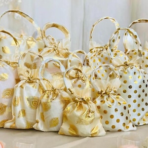 May include: A collection of white satin drawstring bags with gold accents. Some bags feature a peacock feather design, while others have gold polka dots. The bags are perfect for party favors, gifts, or small items.