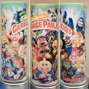 Puede incluir: Un vaso verde y blanco con un gráfico de los personajes de Garbage Pail Kids. Los personajes están en una variedad de poses y expresiones, incluyendo un monstruo, un bebé y una niña con una muñeca. El texto "Garbage Pail Kids" está impreso en letras rojas en el vaso.